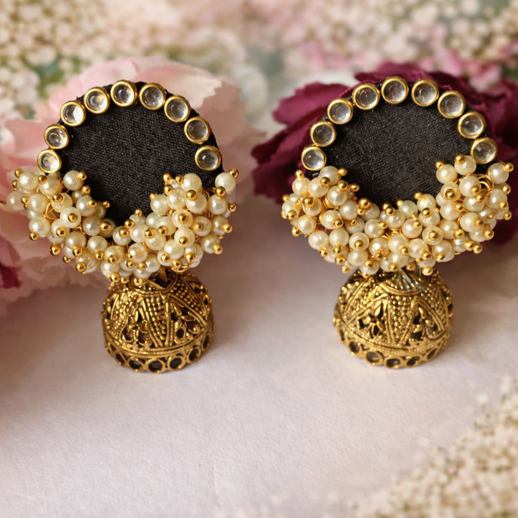 Finished pair of black and gold jhumka earrings photographed on a deep navy stand