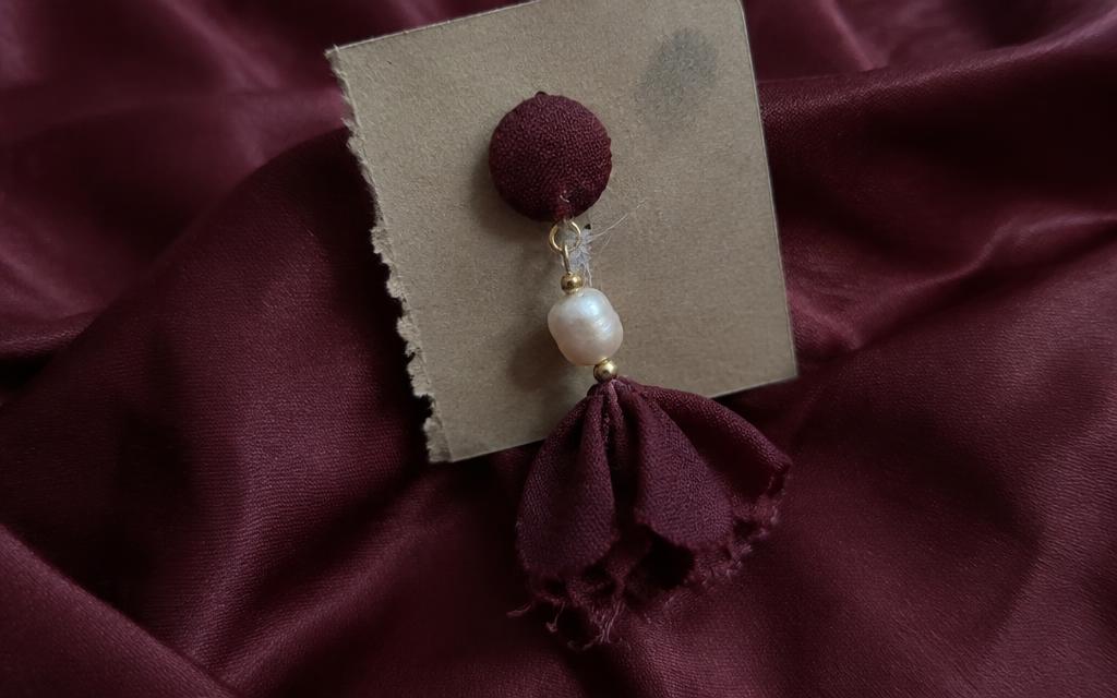 Close-up of a handmade pearl earring with visible glue strings, a crooked pearl and a frayed fabric edge